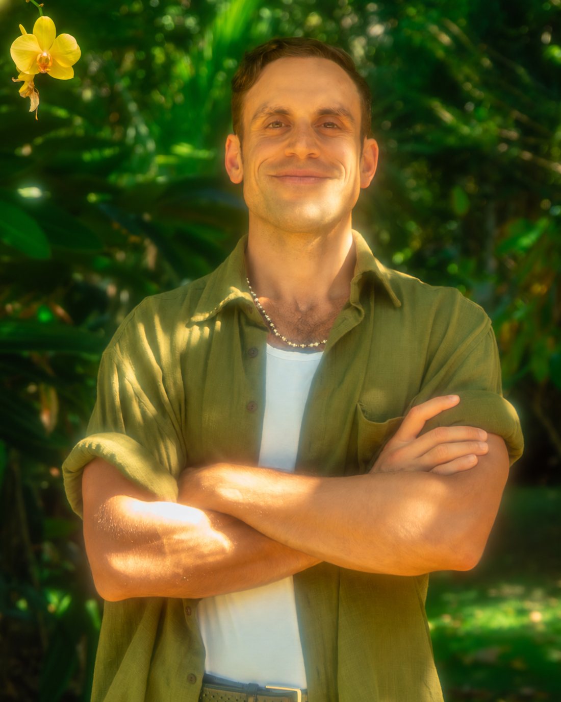 Sid in a green shirt, arms folded, smiling in the jungle light